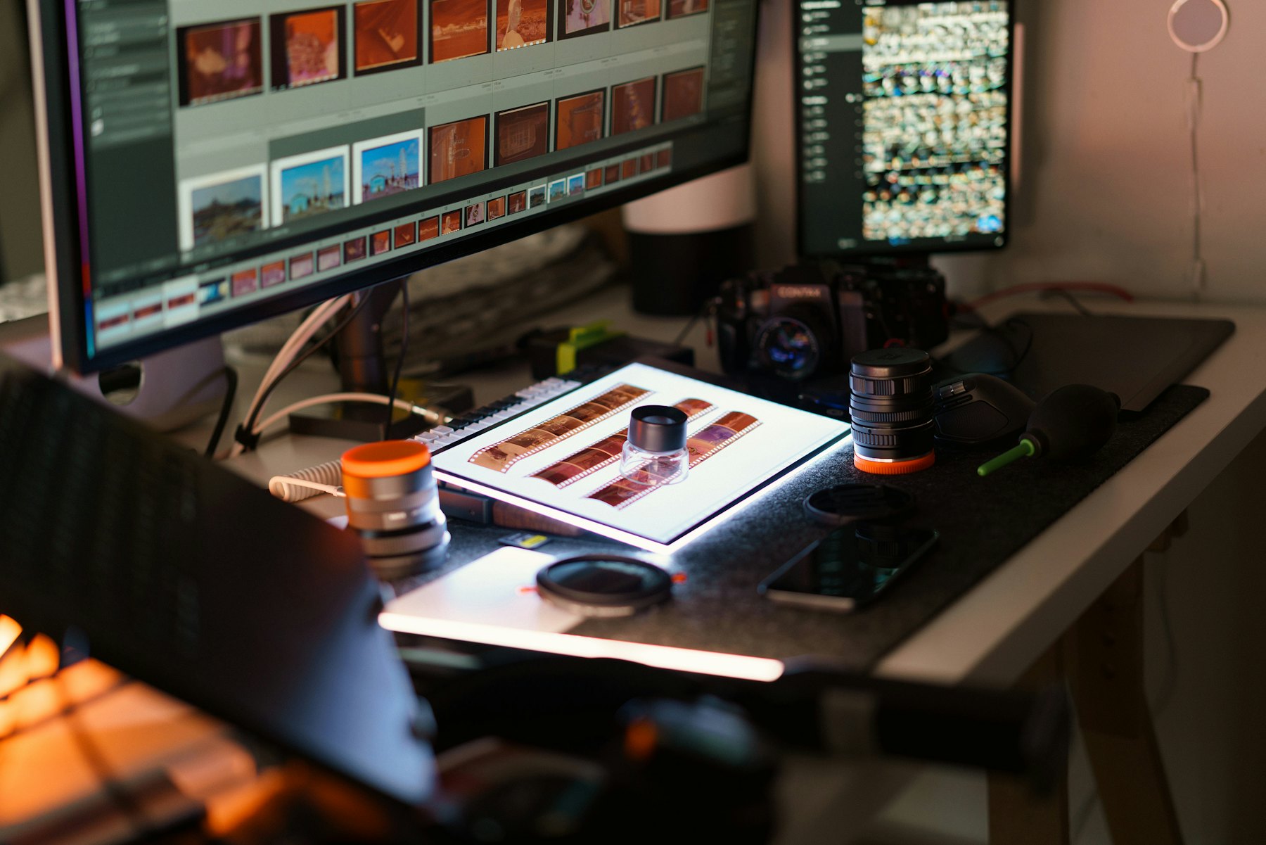Arbeitsplatz mit Monitoren, Kamera und Fotoabzügen
